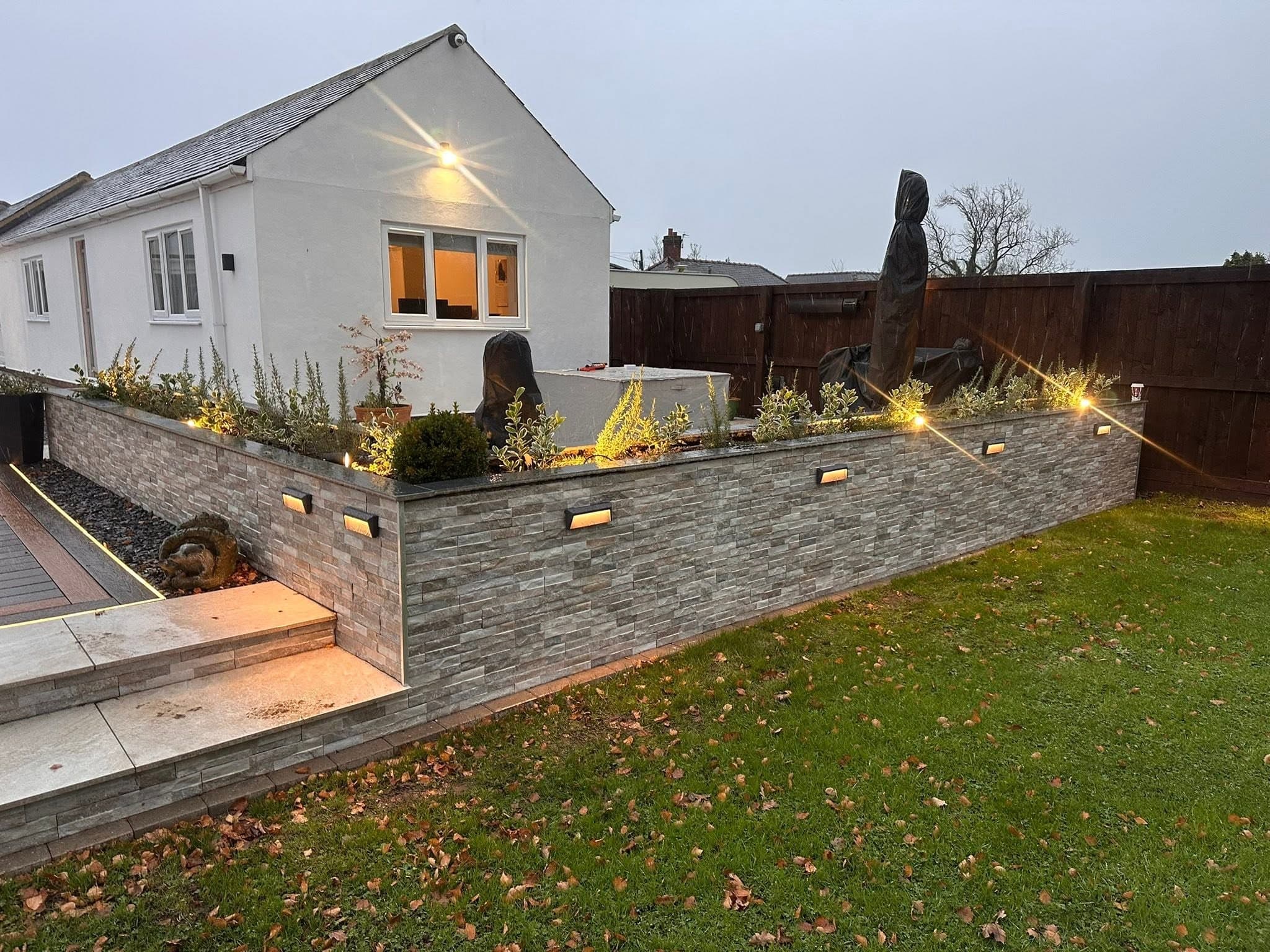 Rendered gable end floodlit at dusk, with recessed lighting picking out the stone-clad retaining wall below