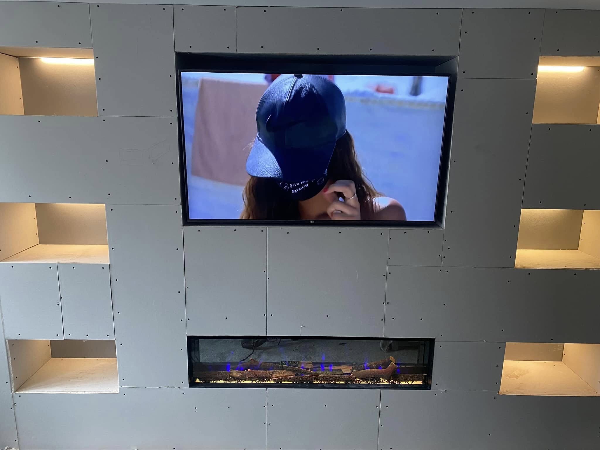 Finished media wall with a wall-mounted television, inset electric fire and warmly lit display niches